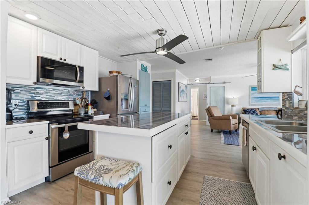 Kitchen featuring decorative backsplash, white cabinets, stainless steel appliances, wood ceiling, and a barn door
