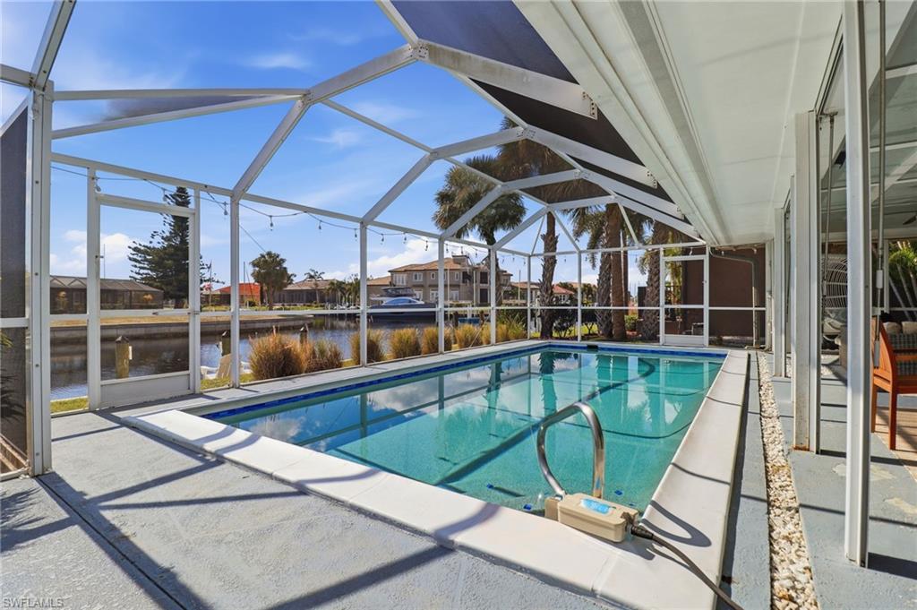 Outdoor pool featuring a sunroom, a patio, glass enclosure, and a water view