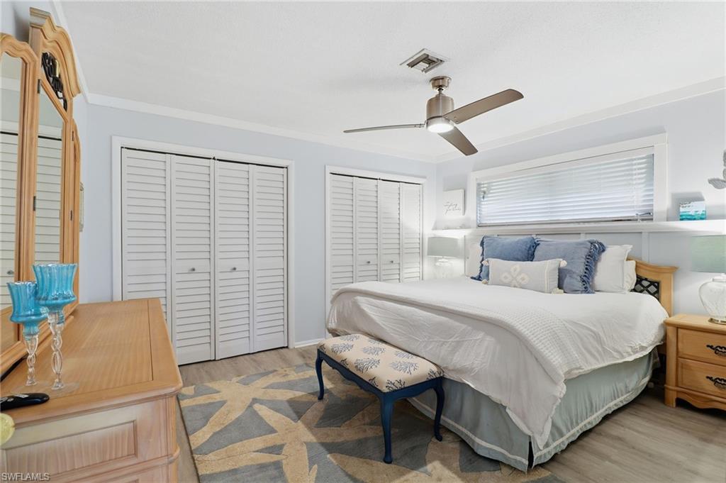 Bedroom with two closets, ceiling fan, light wood-style floors, and crown molding