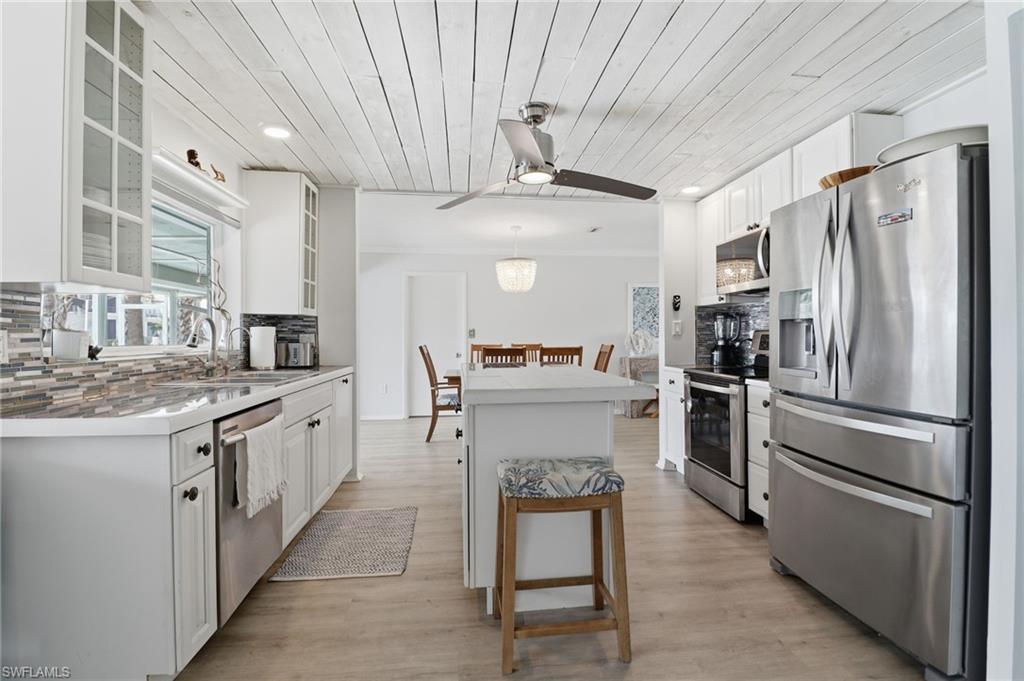 Kitchen with stainless steel appliances, wooden ceiling, white cabinets, decorative backsplash, and hanging light fixtures
