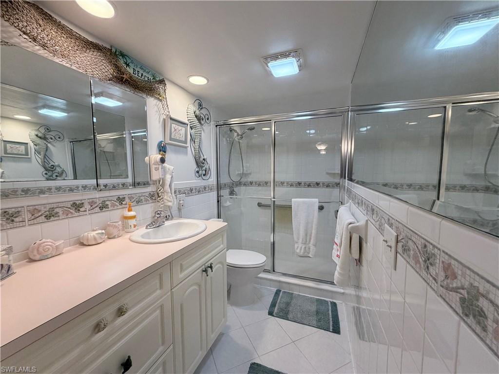 Full bath featuring light tile patterned floors, vanity, a shower stall, and tile walls