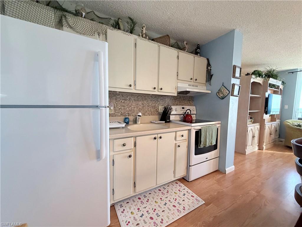 Kitchen featuring white appliances, light countertops, a textured ceiling, under cabinet range hood, and light wood-style flooring