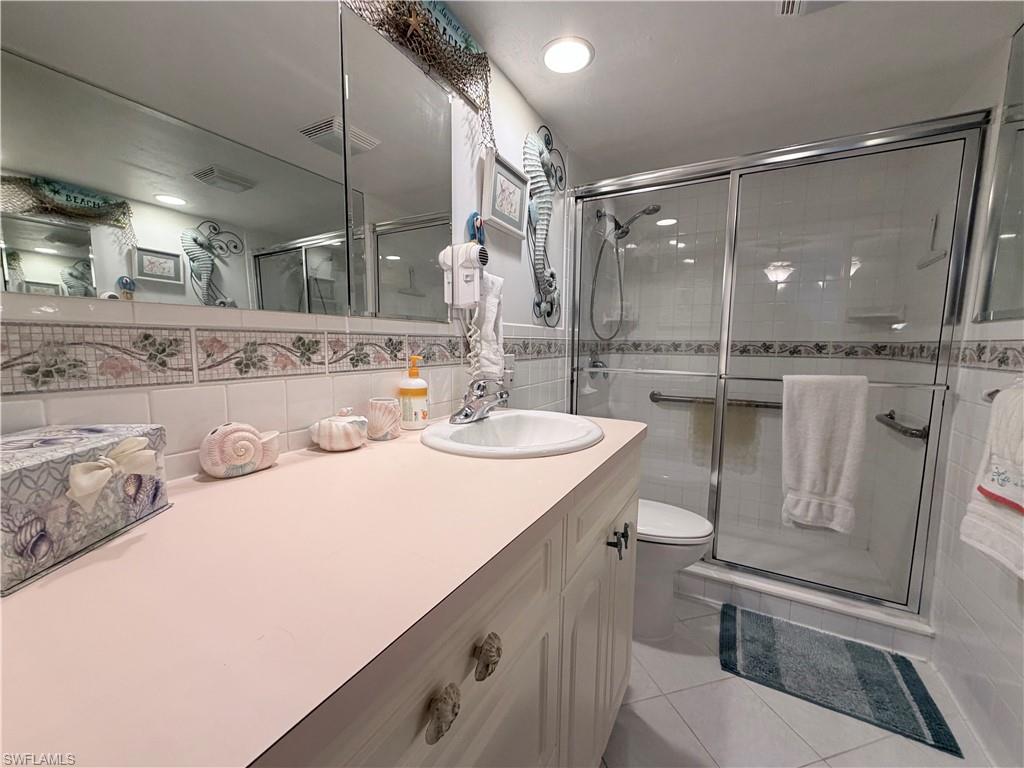 Bathroom featuring vanity, a shower stall, tile walls, light tile patterned floors, and backsplash