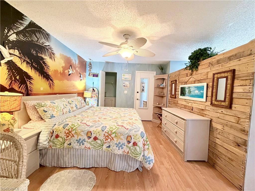 Bedroom featuring wood walls, a textured ceiling, light wood finished floors, and ceiling fan
