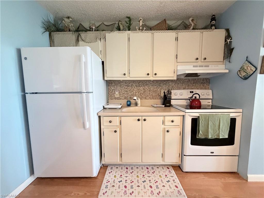 Kitchen featuring white appliances, light countertops, decorative backsplash, under cabinet range hood, and light wood finished floors