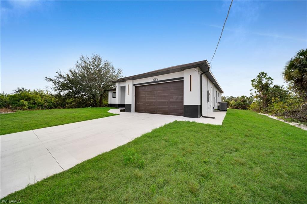 View of front of home featuring driveway, stucco siding, a front yard, and a garage