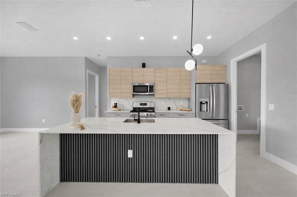 Kitchen with stainless steel appliances, light stone counters, recessed lighting, decorative light fixtures, and light brown cabinets
