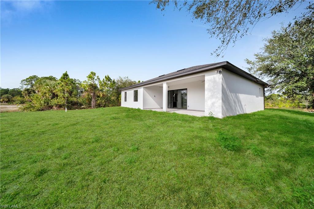 Rear view of house with stucco siding, a patio area, and a yard