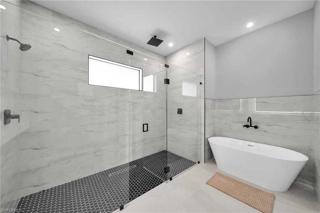 Full bathroom featuring a soaking tub, a marble finish shower, tile walls, and recessed lighting