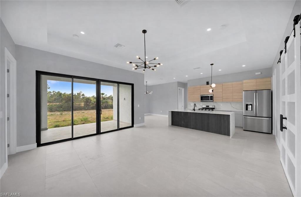 Kitchen with a barn door, pendant lighting, appliances with stainless steel finishes, a chandelier, and open floor plan