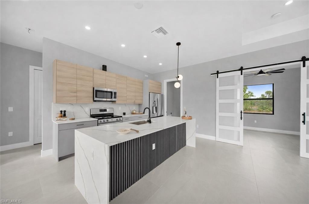 Kitchen featuring a barn door, light brown cabinets, stainless steel appliances, a center island with sink, and recessed lighting
