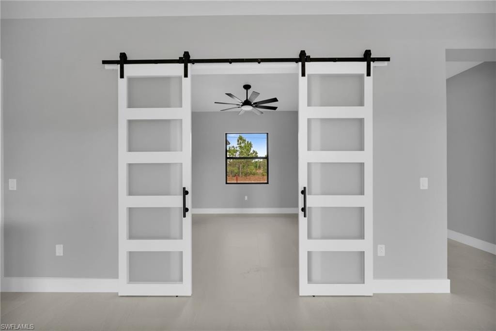 Unfurnished room with a barn door, built in shelves, and a ceiling fan