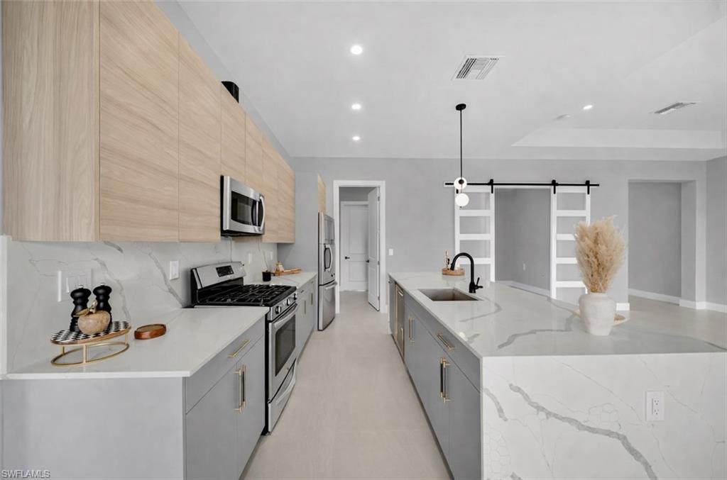 Kitchen with a barn door, stainless steel appliances, modern cabinets, light stone countertops, and a large island
