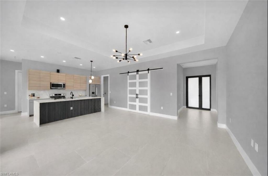 Kitchen featuring a barn door, open floor plan, a large island with sink, a chandelier, and hanging light fixtures