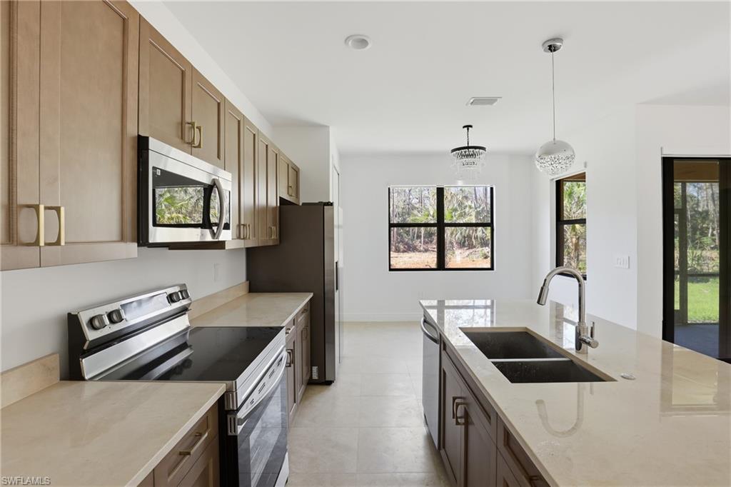 Kitchen with stainless steel appliances, hanging light fixtures, and light stone counters