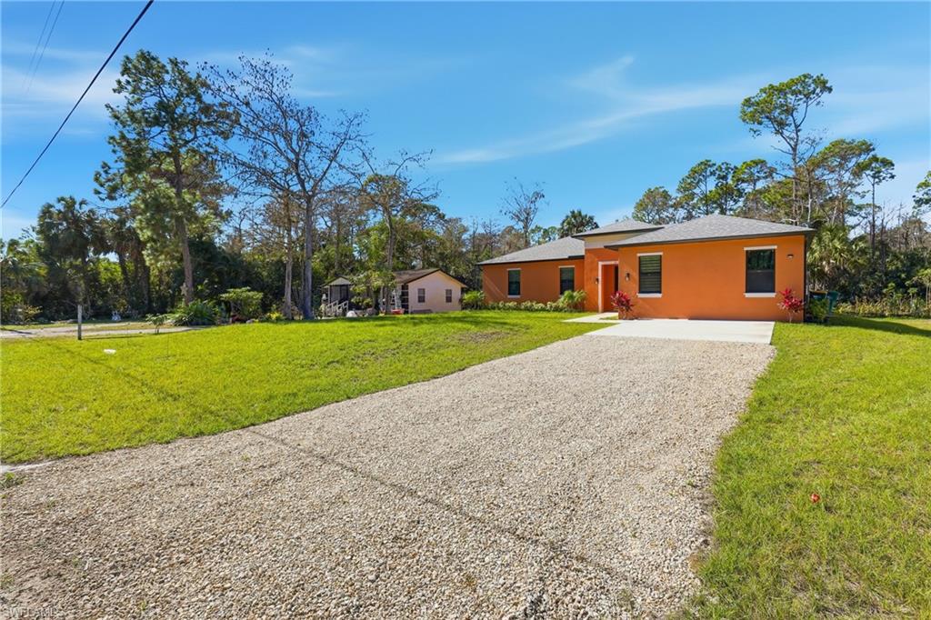 Ranch-style home featuring gravel driveway, a front lawn, and stucco siding
