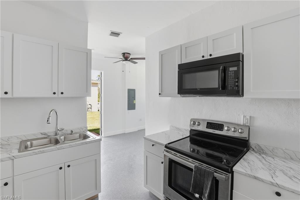 Kitchen with electric range, black microwave, and white cabinetry