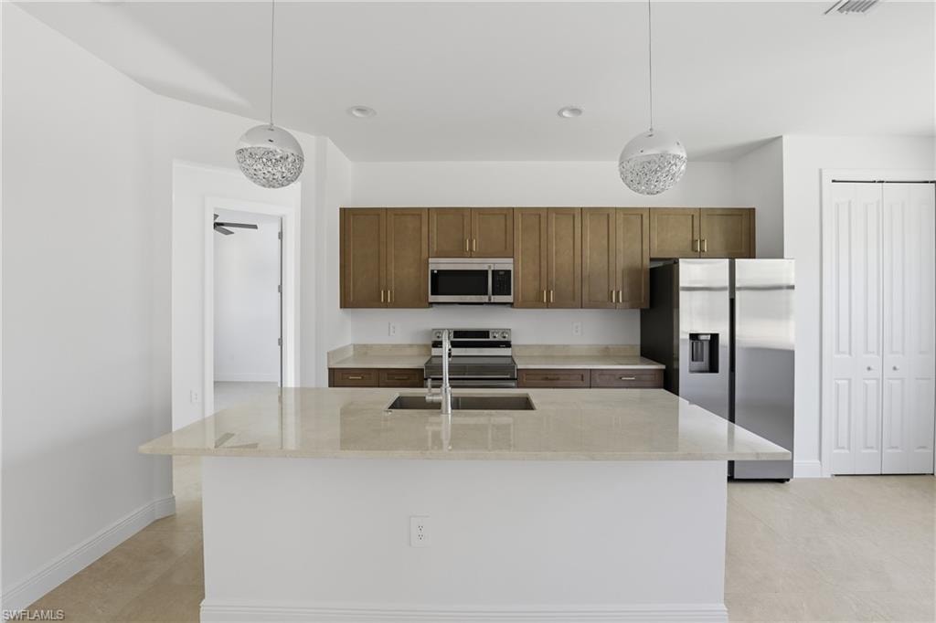Kitchen with appliances with stainless steel finishes, light stone counters, a kitchen island with sink, pendant lighting, and recessed lighting