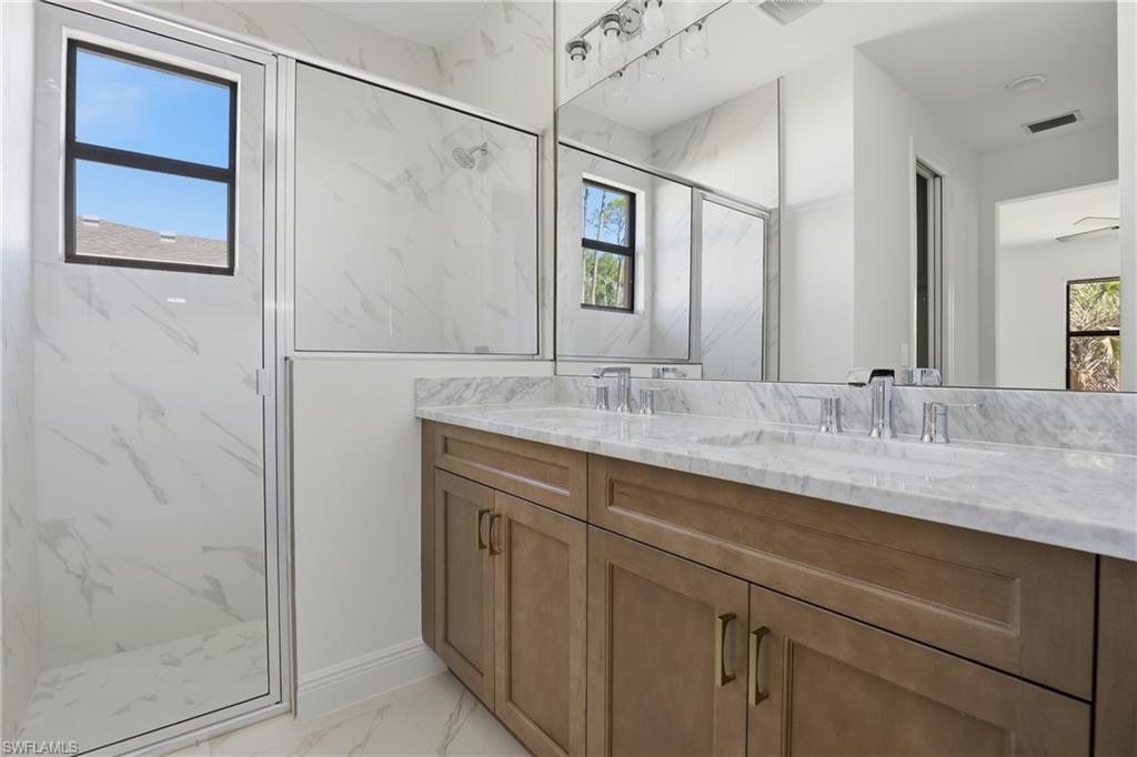 Full bathroom featuring double vanity, light marble finish floors, and a marble finish shower