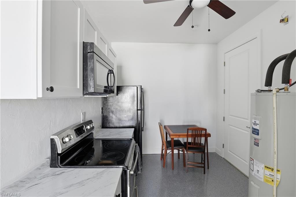 Kitchen with stainless steel range with electric cooktop, black microwave, water heater, white cabinets, and a ceiling fan