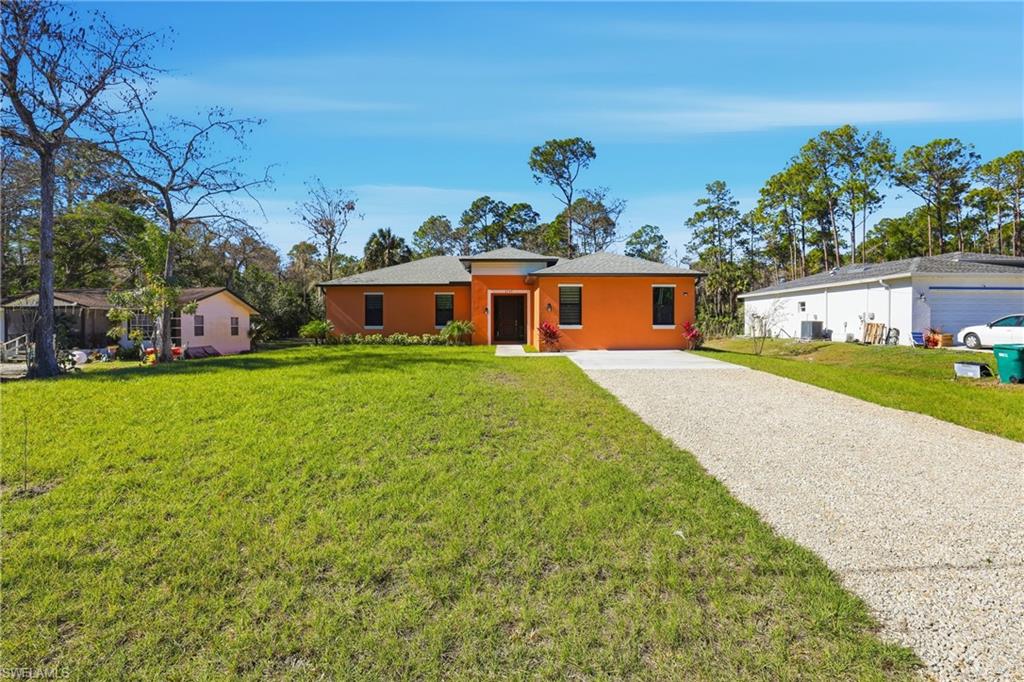 View of front of house with a front yard, stucco siding, and gravel driveway