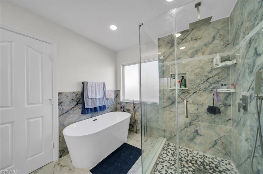 Bathroom with a soaking tub, tile walls, a marble finish shower, marble tiled flooring, and a wainscoted wall