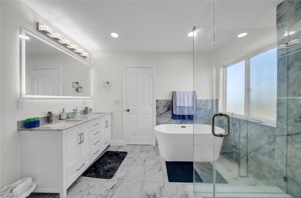 Bathroom with a soaking tub, double vanity, light marble finish flooring, a marble finish shower, and recessed lighting
