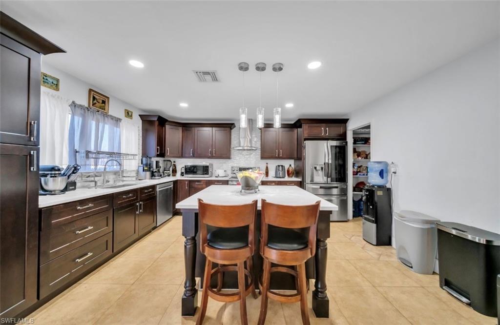 Kitchen with a breakfast bar, stainless steel appliances, dark brown cabinets, decorative light fixtures, and a kitchen island