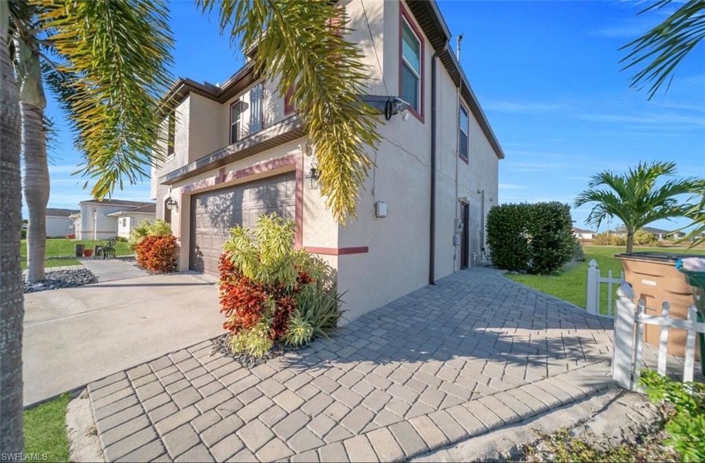 View of side of property featuring stucco siding, a garage, driveway, and a lawn