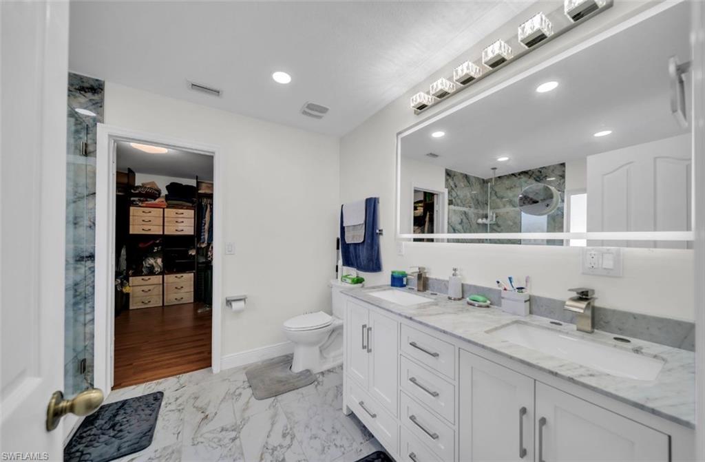 Bathroom featuring a marble finish shower, a walk in closet, light marble finish flooring, double vanity, and recessed lighting