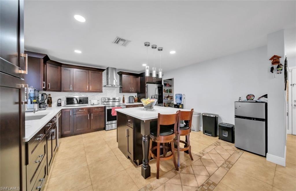 Kitchen with light tile patterned floors, stainless steel appliances, a kitchen bar, a kitchen island, and dark brown cabinetry