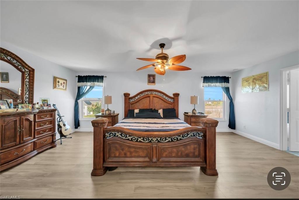 Bedroom with a ceiling fan, light wood-style flooring, and multiple windows