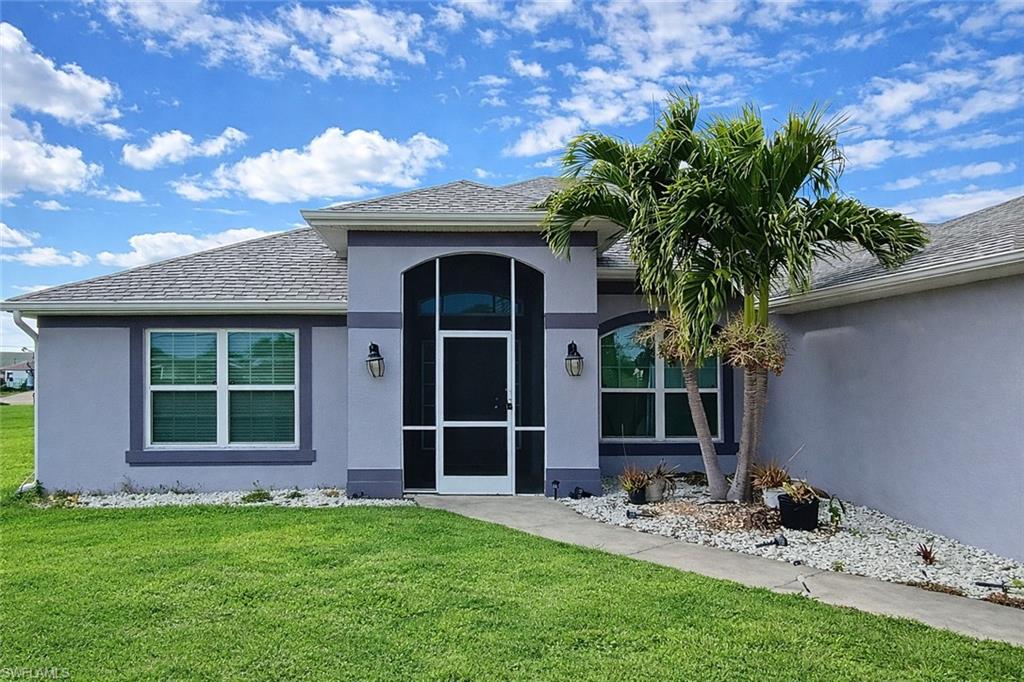 Entrance to property with a yard, stucco siding, a sunroom, and a shingled roof