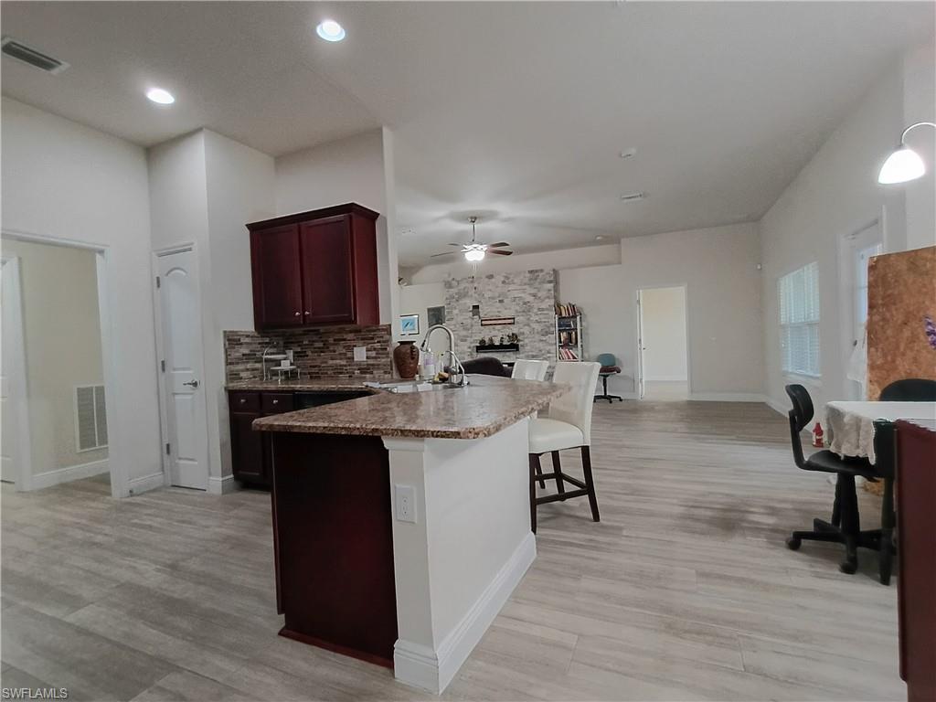 Kitchen featuring a peninsula, a stone fireplace, a kitchen breakfast bar, light wood-style flooring, and recessed lighting