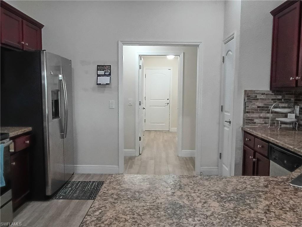 Kitchen featuring dark stone counters, backsplash, appliances with stainless steel finishes, and light wood-style flooring