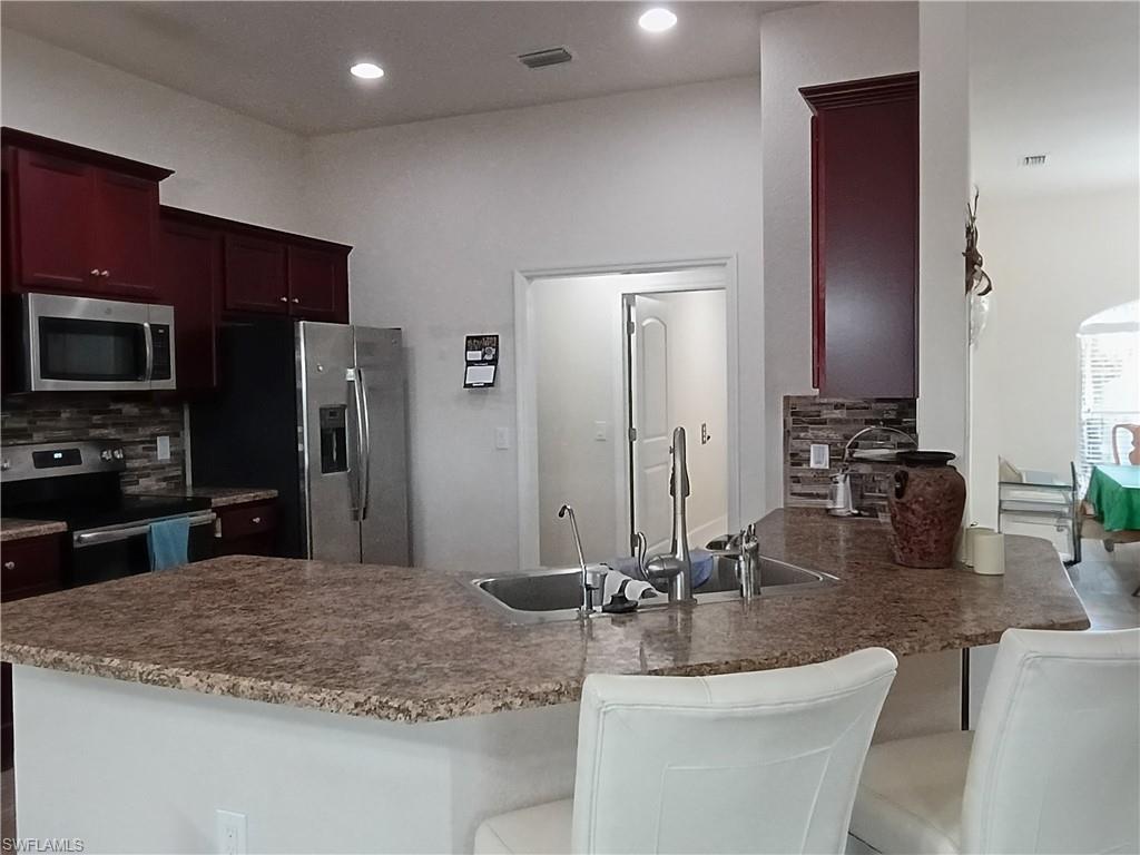 Kitchen featuring appliances with stainless steel finishes, a peninsula, a kitchen breakfast bar, dark brown cabinets, and tasteful backsplash