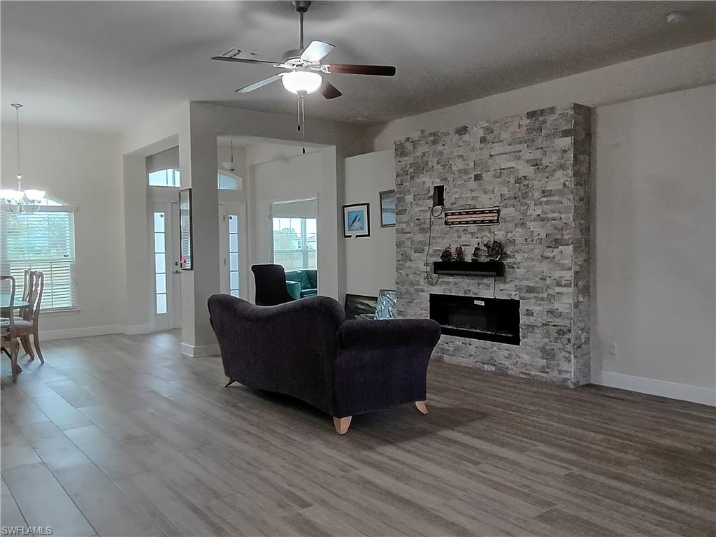Living area featuring ceiling fan, wood finished floors, a stone fireplace, and a chandelier