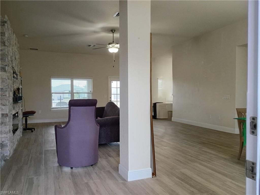 Living area featuring light wood-type flooring, ceiling fan, and a stone fireplace