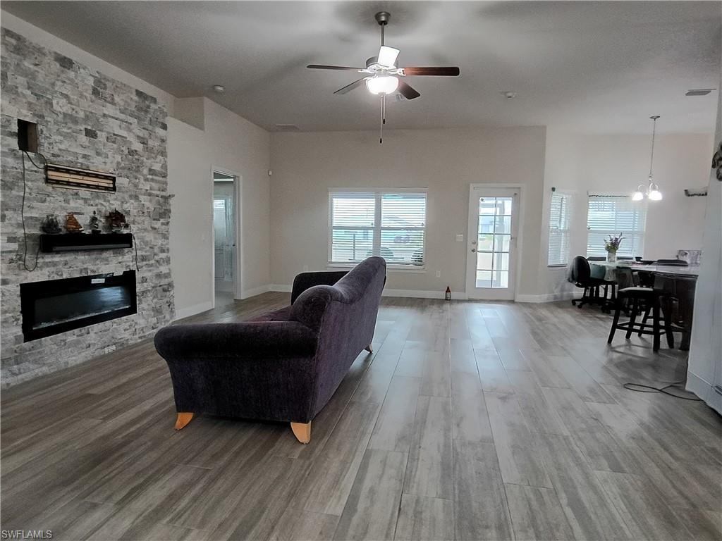 Living room featuring a stone fireplace, a ceiling fan, light wood finished floors, and a chandelier