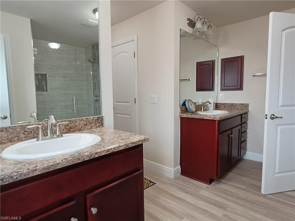 Full bathroom featuring a shower stall, two vanities, and light wood-style flooring