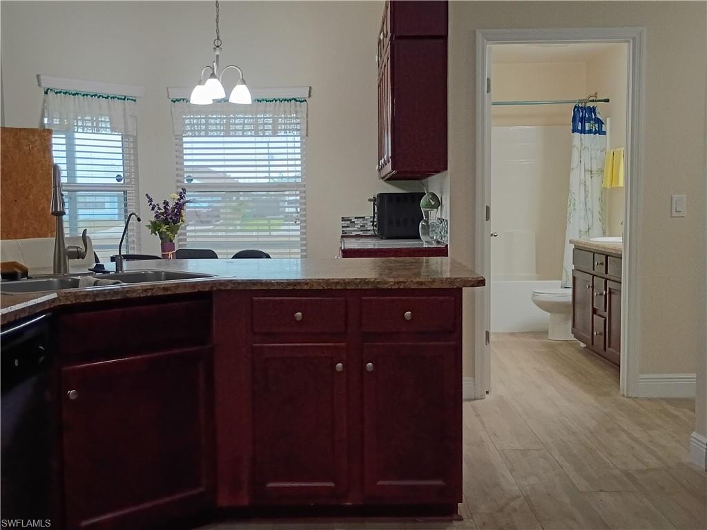 Kitchen featuring reddish brown cabinets, pendant lighting, black dishwasher, and light wood-style flooring
