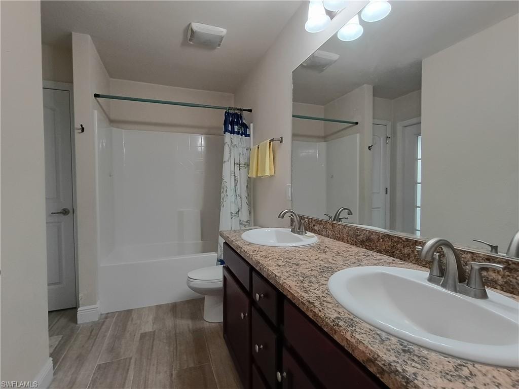 Bathroom with double vanity, shower / tub combo with curtain, and light wood-type flooring