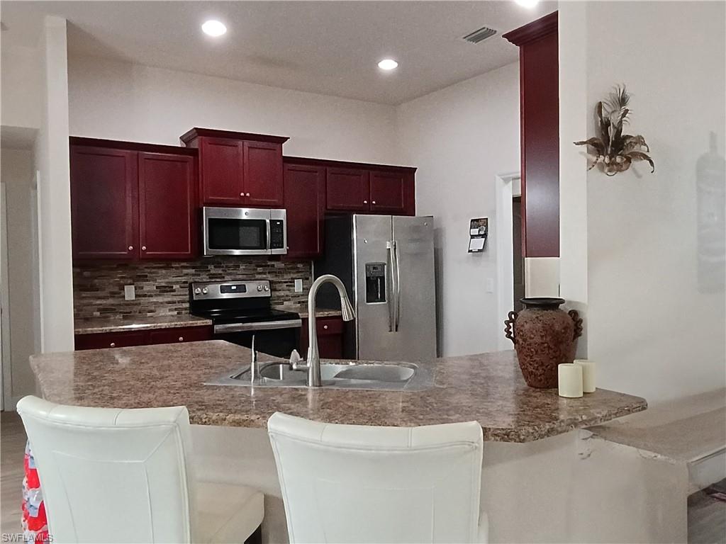 Kitchen featuring dark brown cabinets, appliances with stainless steel finishes, a kitchen bar, a peninsula, and tasteful backsplash