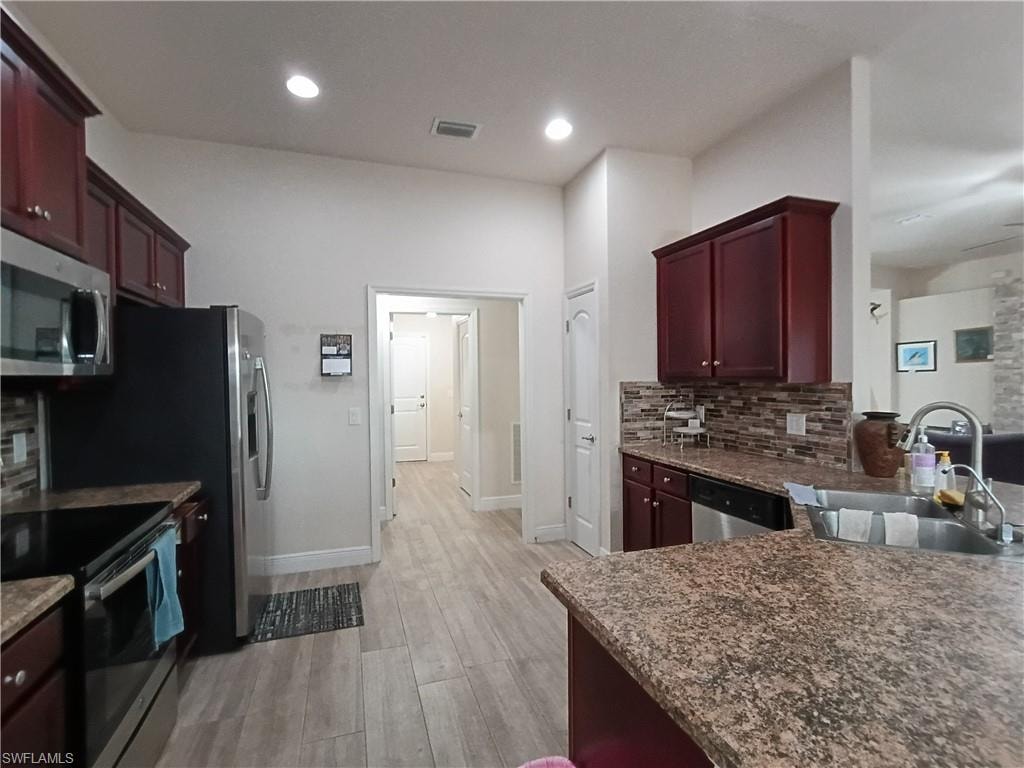 Kitchen with reddish brown cabinets, backsplash, stainless steel appliances, dark stone counters, and recessed lighting