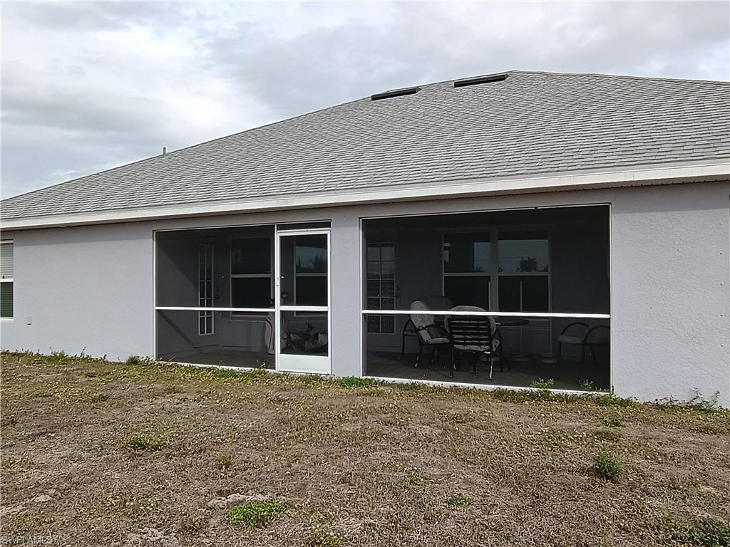 Back of house with stucco siding, a sunroom, and a shingled roof