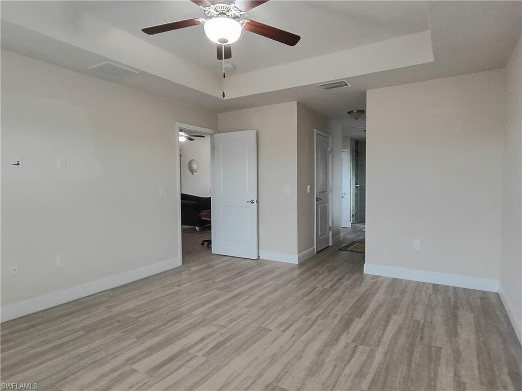 Unfurnished bedroom featuring a tray ceiling, a ceiling fan, and light wood finished floors