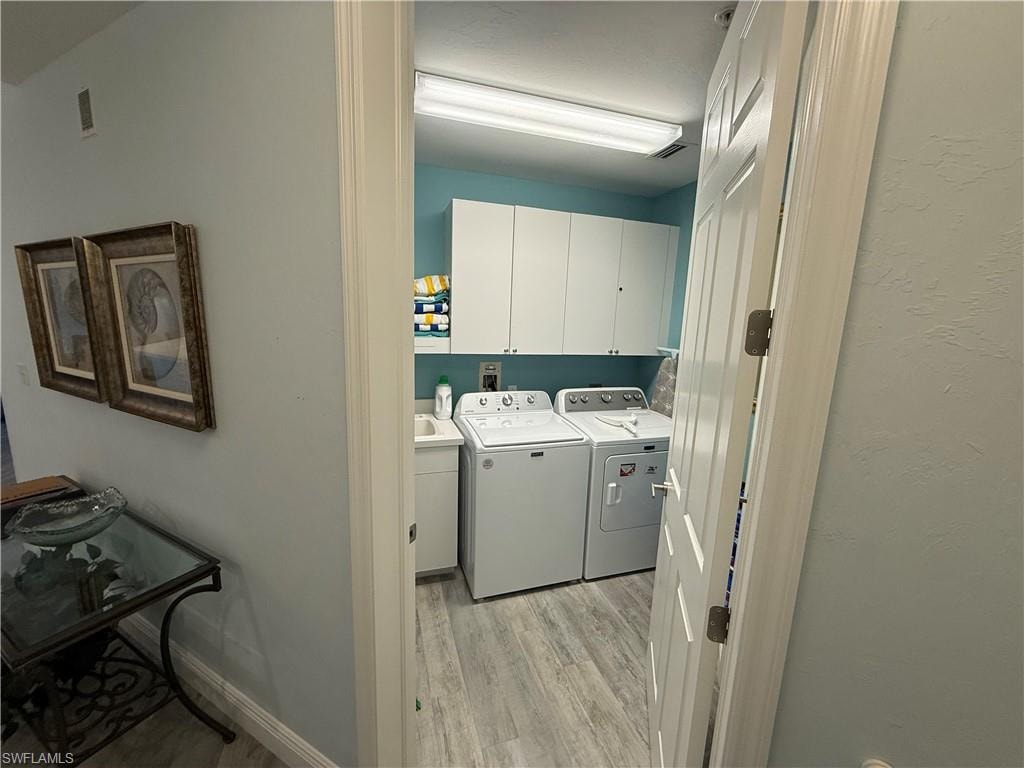Laundry room featuring cabinet space, washing machine and clothes dryer, light wood-style floors, and a textured wall