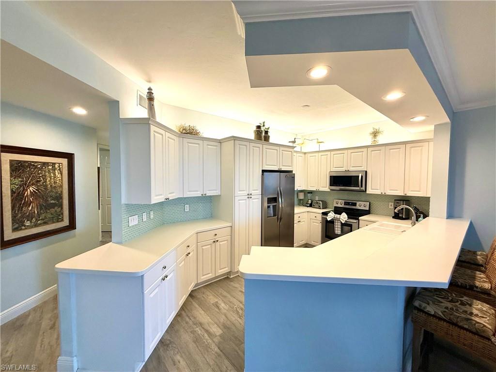 Kitchen with a peninsula, appliances with stainless steel finishes, light countertops, backsplash, and recessed lighting