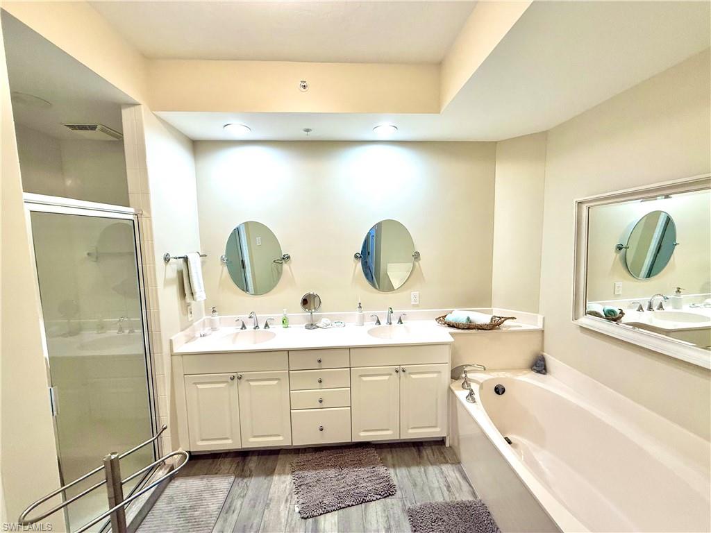 Full bathroom featuring double vanity, a garden tub, a shower stall, and light wood-type flooring