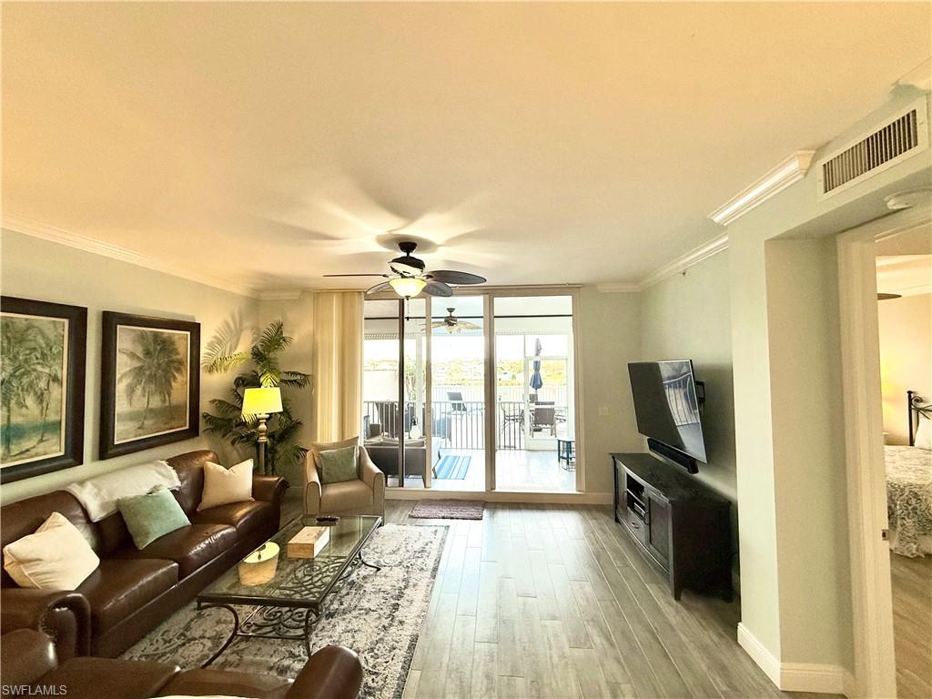 Living area with ornamental molding, a ceiling fan, light wood-style floors, and a wall of windows